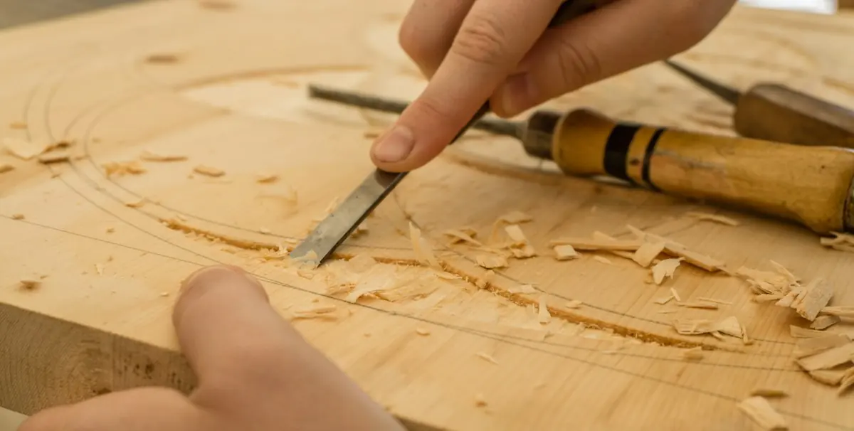 Mit dem Stechbeitel wird entlang einer Bleistiftlinie ein Bogen in eine helle Holzplatte gestochen